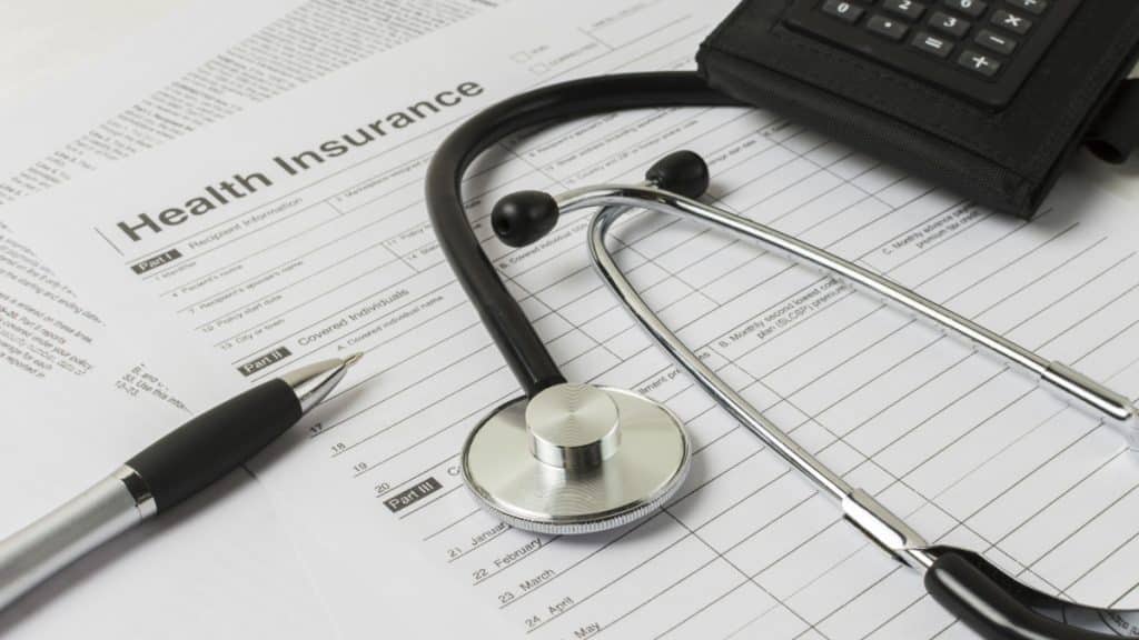 un stéthoscope est posé sur un contrat d'assurance à côté d'une calculatrice noire.